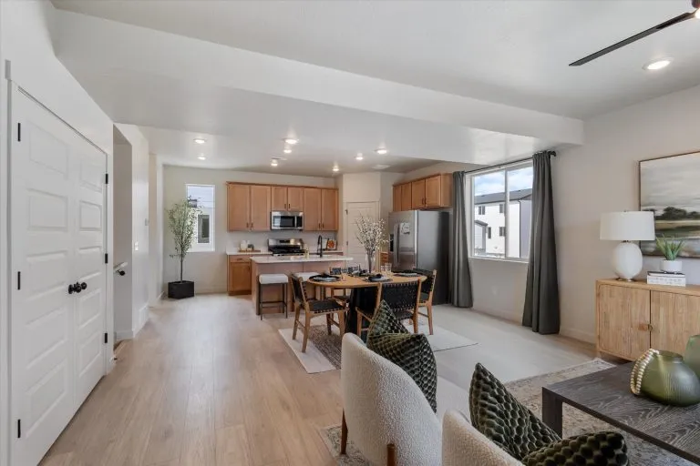 Open-concept modern kitchen and dining area with light wood floors, stainless steel appliances, a dining table set for four, neutral decor, large windows, and stylish contemporary furnishings.