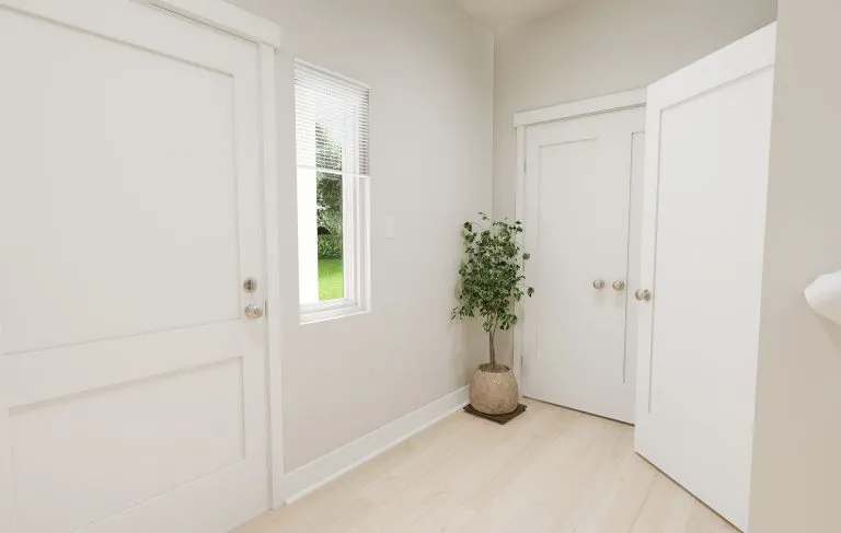 A bright, minimalist room with light wood flooring, white doors, a small window revealing green grass outside, and a potted plant in the corner near a double-door closet—perfectly capturing the airy style of modern homes in Utah.