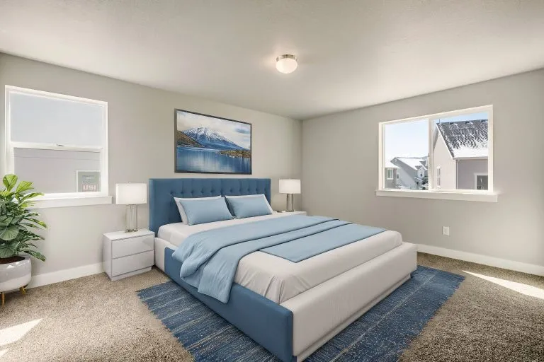 A modern bedroom with a large blue bed, matching bedding, two white nightstands with lamps, a potted plant, and two windows showing homes in Utah outside. A mountain landscape painting hangs above the bed.