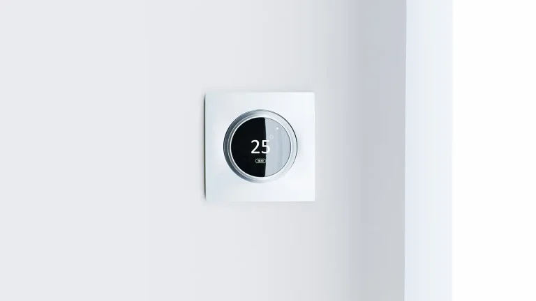 Round smart thermostat mounted on a white wall displaying 25 degrees, an energy-saving feature found in modern new construction homes.