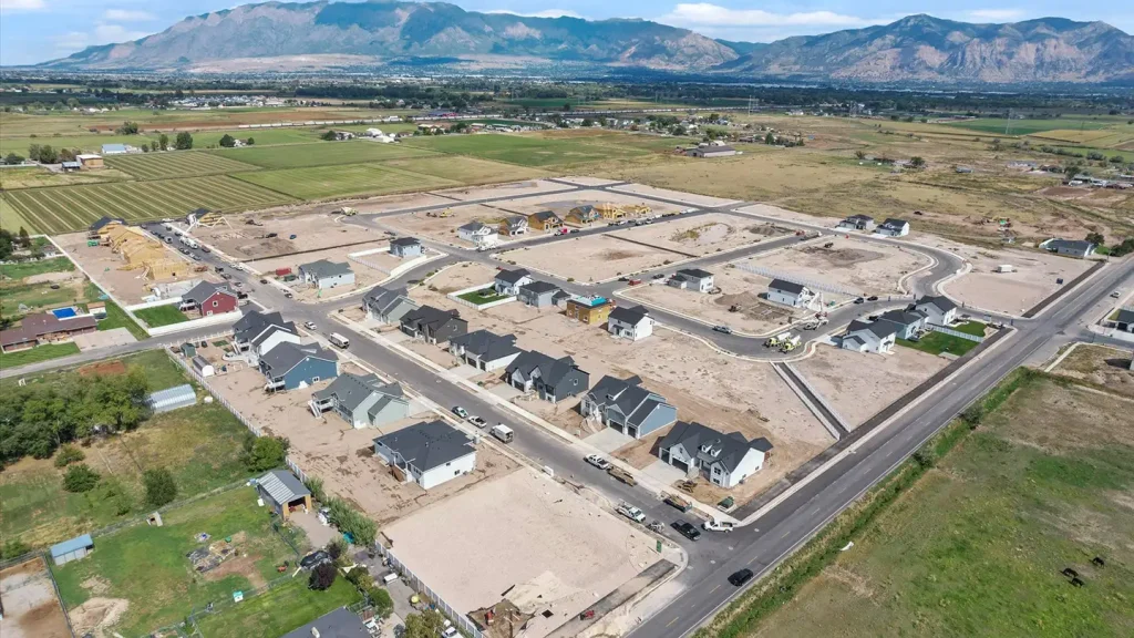 Aerial view of a new home development in progress with completed homes, dirt lots under construction, and mountains beyond.