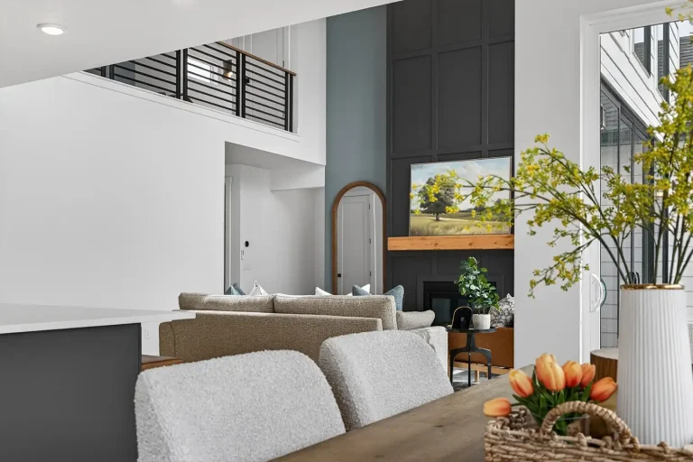 Two-story living room with vaulted ceiling, dark board-and-batten fireplace wall, framed landscape art, and neutral gray sofa seating.